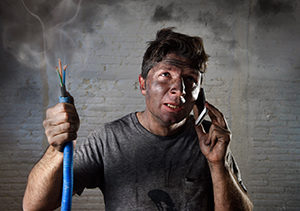 Man on cellphone covered in soot holding smoking electrical wires