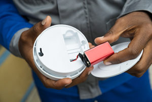 Man showing holding 9V battery and smoke detector